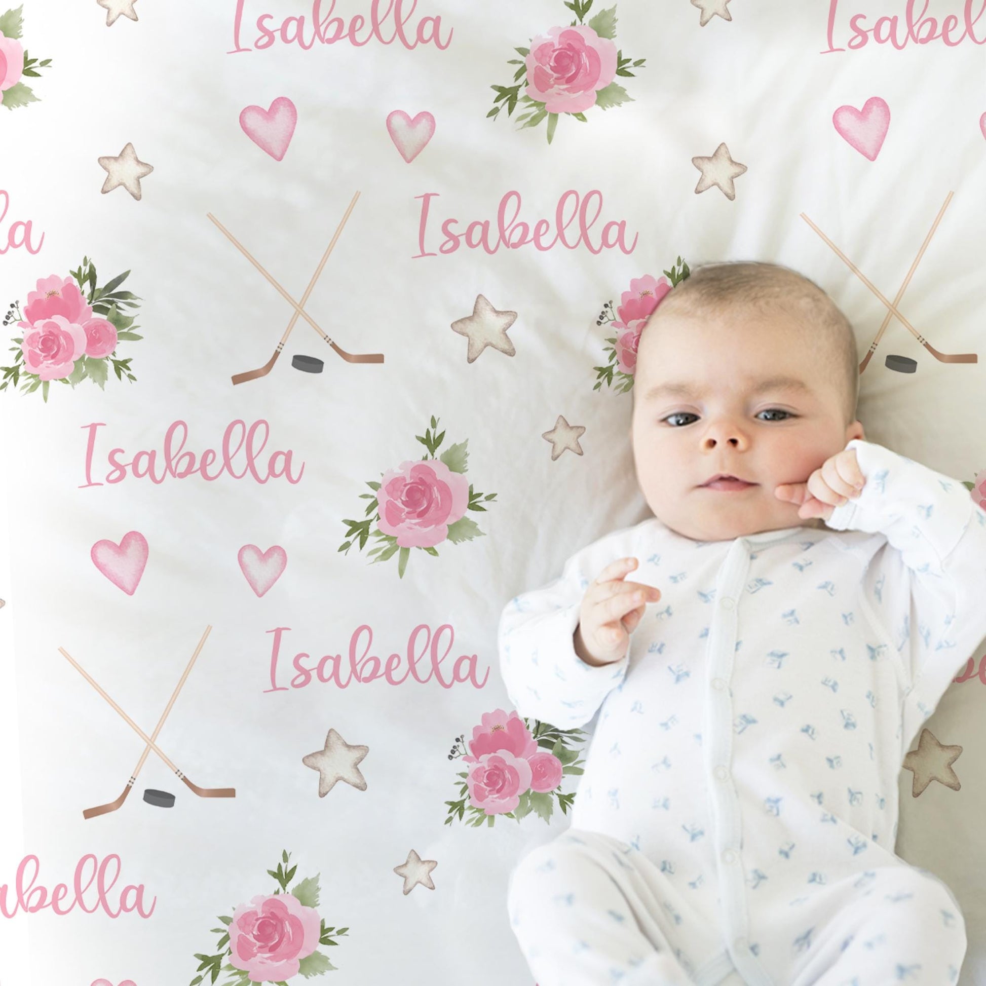 Baby laying on blanket with hockey sticks, puck, and personalized with baby's name in pink.