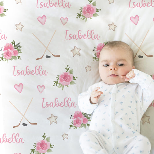 Baby laying on blanket with hockey sticks, puck, and personalized with baby's name in pink.