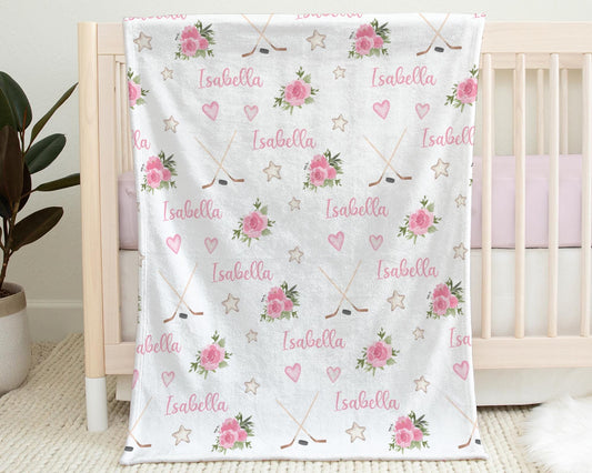 Blanket with hockey sticks, puck, and personalized with baby's name in pink hanging on the side a a crib.
