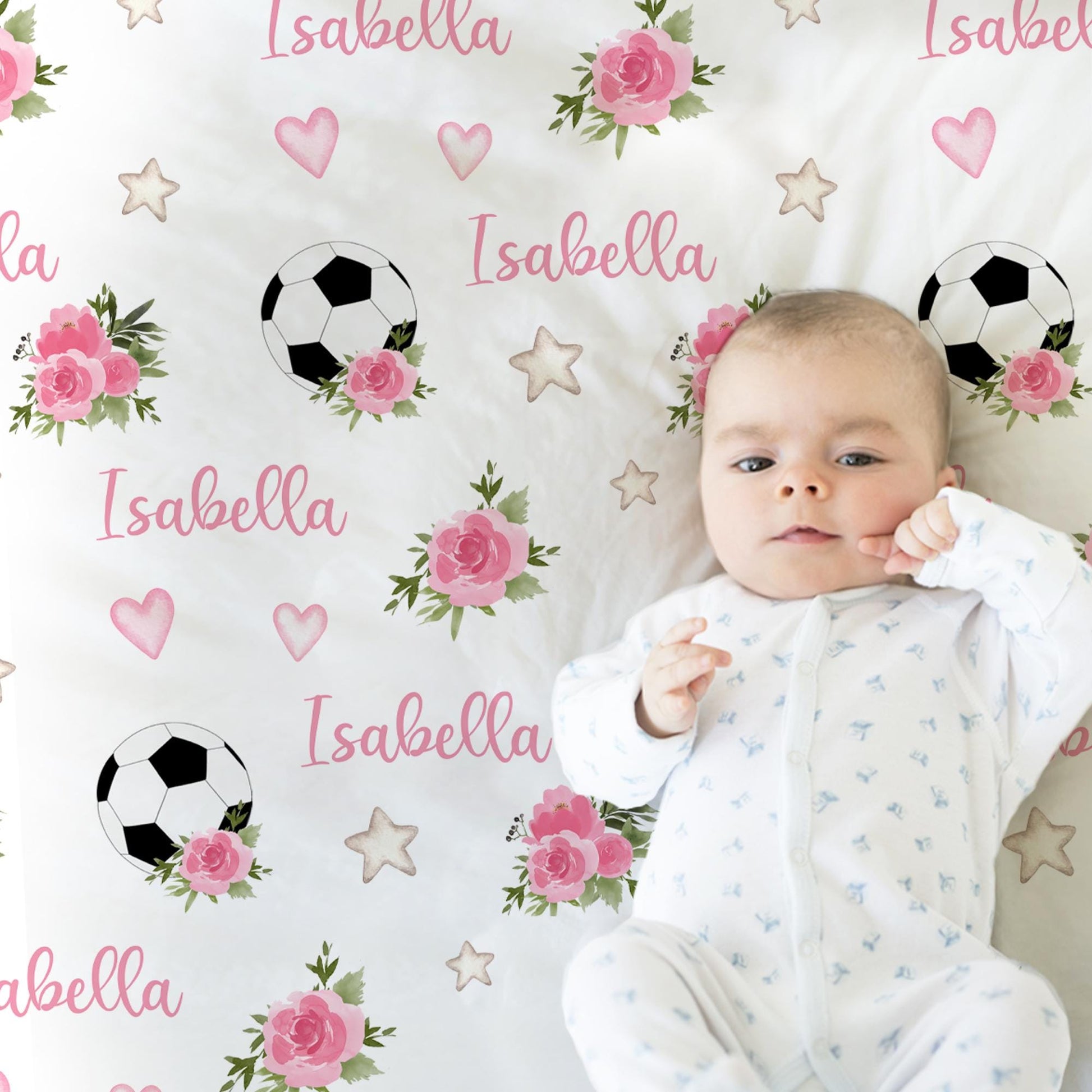 Baby pictured on blanket with soccer balls, pink flowers, and baby's name with hearts and stars.