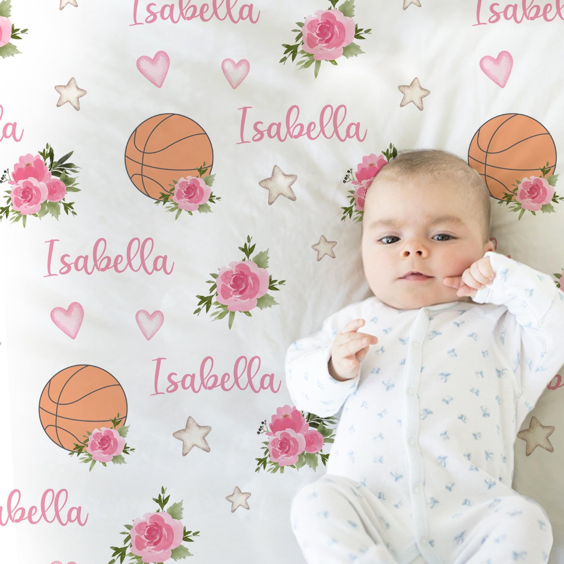 Baby laying on blanket with basketballs and pink flowers that is personalized with baby's name in pink.