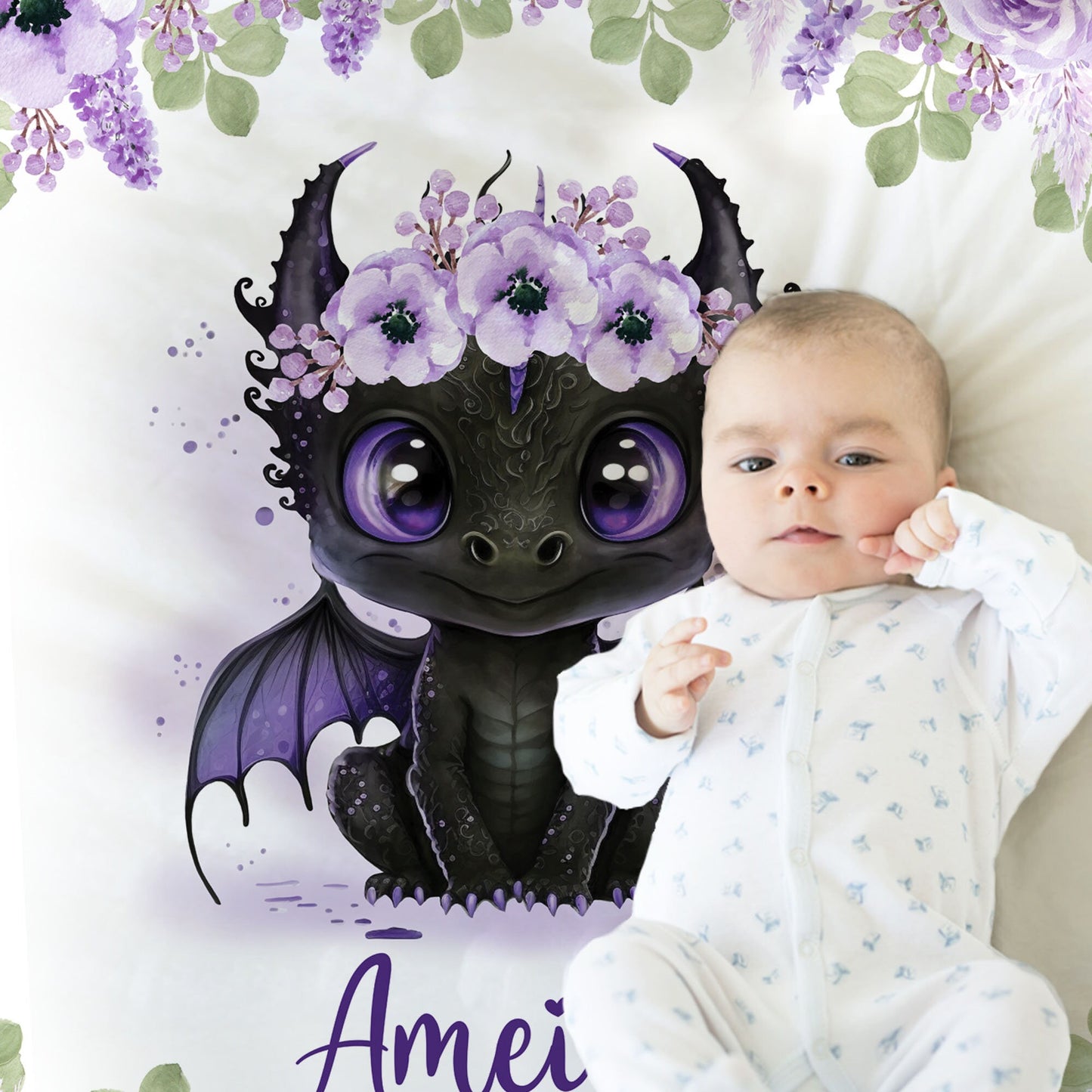 Close up of baby laying on blanket with an image of cute baby dragon with purple flowers on her head.
