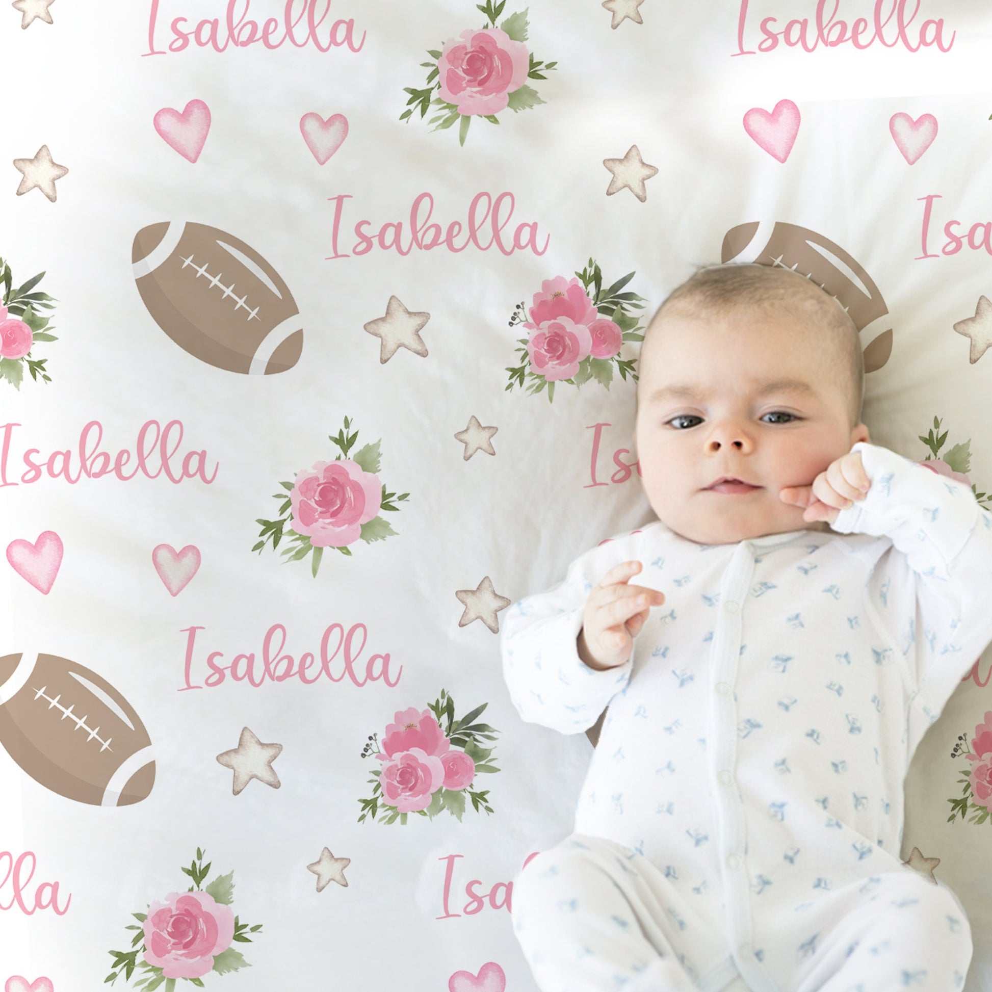 Close up of baby laying on blanket with footballs and pink flowers and personalized with baby's name in pink.