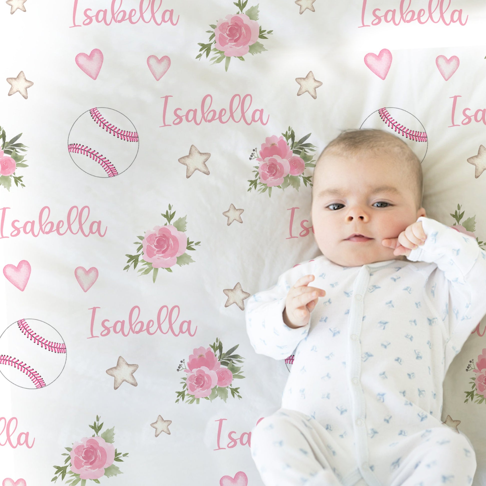 Close up of baby laying on a blanket with baseballs with pink stitching and pink flowers and personalized with baby's name in pink.