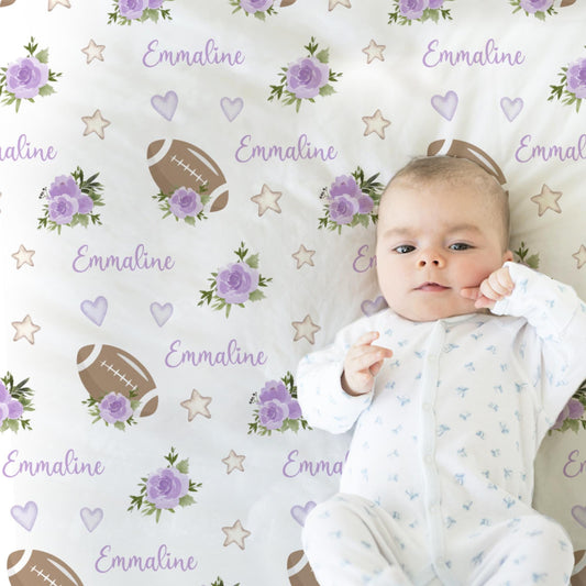 Close up of baby laying on a blanket with footballs and purple flowers and personalized with baby's name in pink.